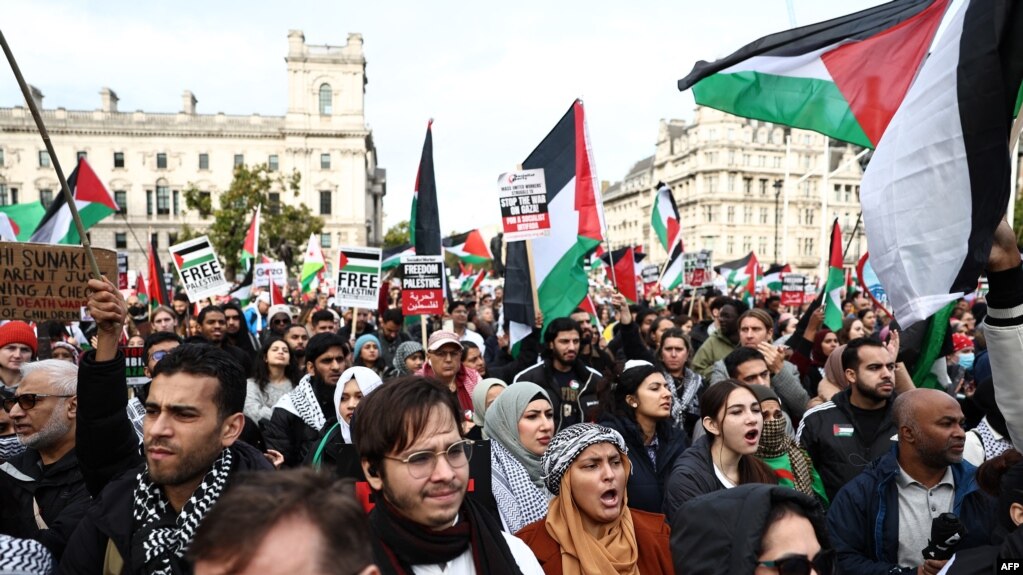 2023年10月28日，人们在伦敦参加“巴勒斯坦游行”后，在议会广场举着标语牌并挥舞巴勒斯坦国旗，呼吁以色列和哈马斯之间的冲突停火。(photo:VOA)