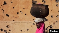 A girl walks by a building pockmarked with bullet holes from fighting in Gao, Mali, Mar. 13 2013. 