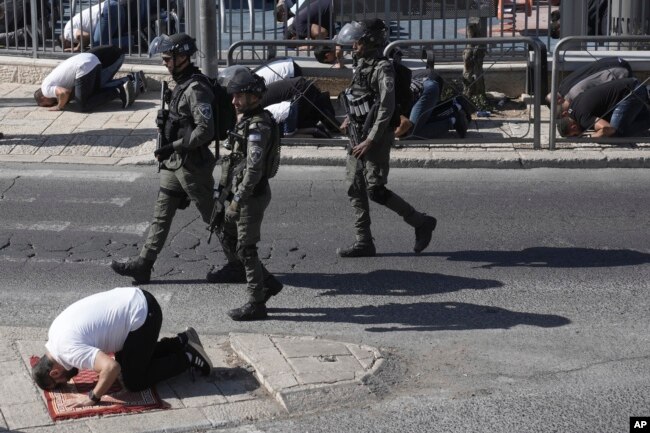 Polisi Israel berpatroli ketika seorang jemaah Muslim, yang dilarang memasuki kompleks Masjid Al Aqsa, salat di depan Kota Tua Yerusalem, 10 November 2023. (Foto: Mahmoud/AP Photo)