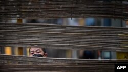 A man wearing a face mask looks through a barrier in a neighborhood in Wuhan, the central Chinese city where the coronavirus first appeared last year, in central Hubei province.