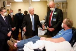 FILE - Vice President Mike Pence, center, visits Dennis Nelson, a patient who survived the coronavirus and was going to give blood, during a tour of the Mayo Clinic, in Rochester, Minn., April 28, 2020.