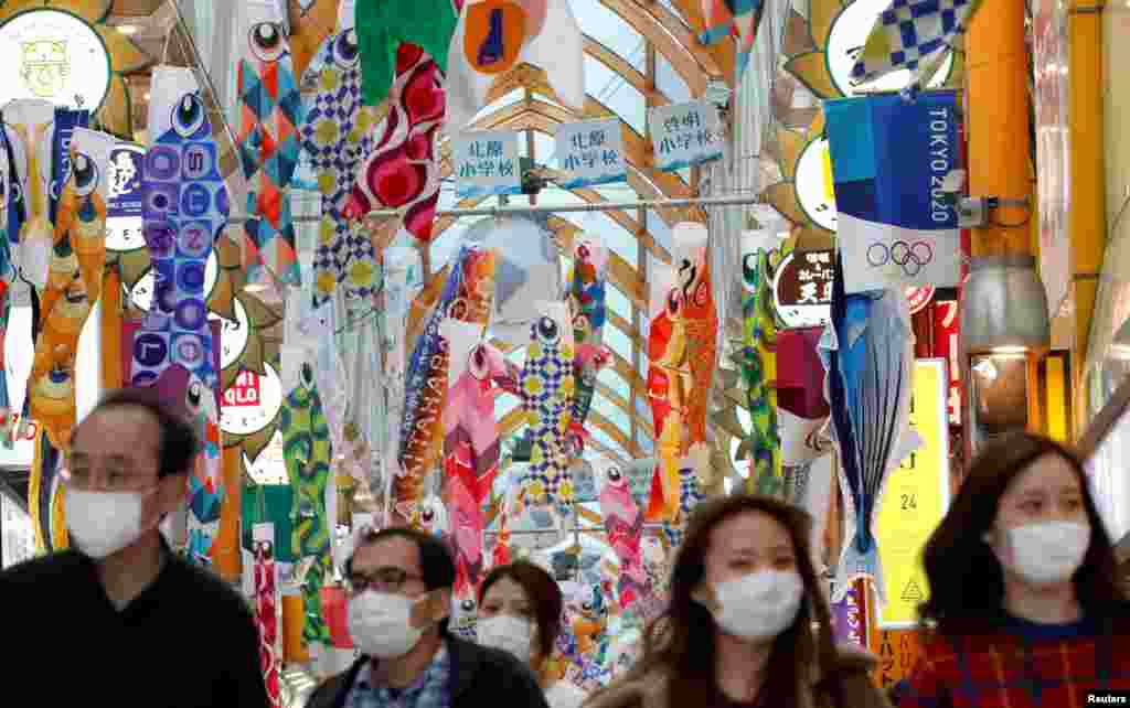 People wearing face masks walk under fluttering Koinobori, traditional Japanese carp-shaped windsocks that are hung in Japan from April to early May to wish a good health for children, following the coronavirus outbreak, in Tokyo, Japan.