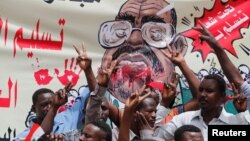 2019年4月19日，抗议者在苏丹喀土穆国防部门前拉着画有前苏丹总统奥马尔·巴希尔的横幅喊口号。