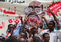 FILE - Protesters shout slogans by a banner depicting former Sudanese President Omar al-Bashir, in front of the Defense Ministry in Khartoum, Sudan, April 19, 2019.