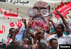 FILE - Protesters shout slogans by a banner depicting former Sudanese President Omar al-Bashir, in front of the Defense Ministry in Khartoum, Sudan, April 19, 2019.