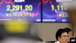 A currency trader watches the computer monitors near the screens showing the Korea Composite Stock Price Index (KOSPI), left, and the foreign exchange rate between U.S. dollar and South Korean won at the foreign exchange dealing room in Seoul, South Korea