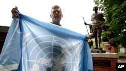 Lewis Randa, of Duxbury, Mass., displays a United Nations flag while standing near a bronze statue of Indian independence leader Mahatma Gandhi, behind right, at the Pacifist Memorial, in Sherborn, Mass. 