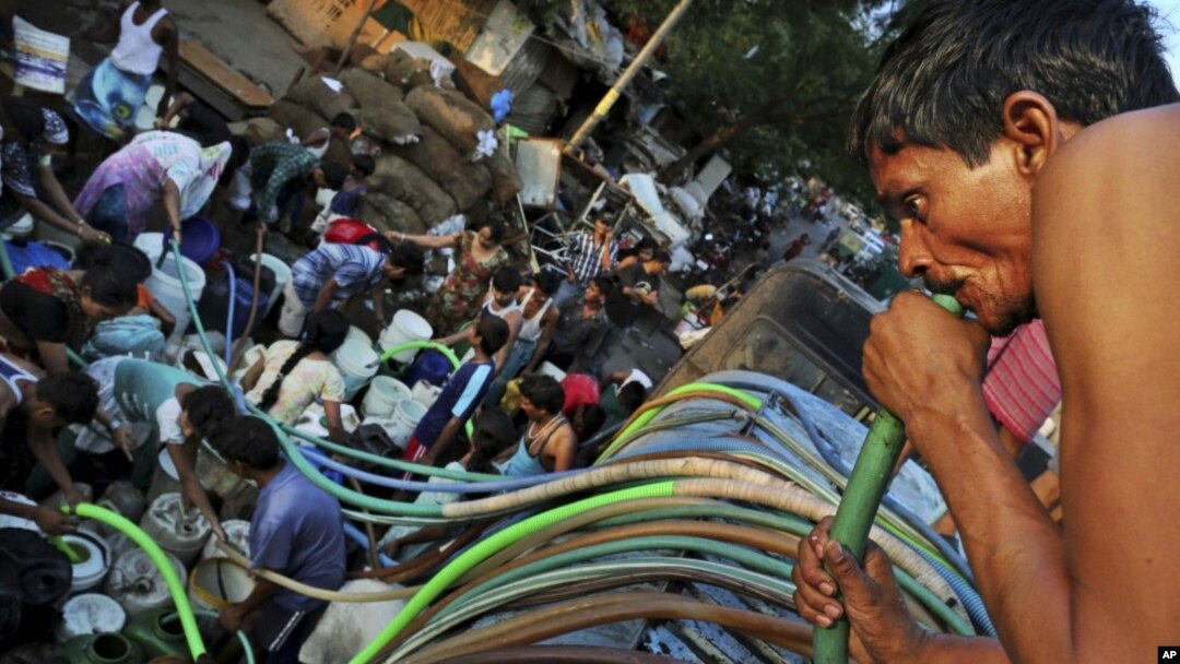 Seorang warga New Delhi mengisap air dari selang sementara yang lainnya mengantri air akibat kekeringan di kota itu. (Foto: AP)