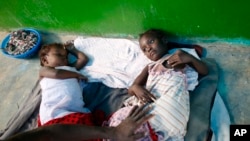 A father comforts his daughter as she receives treatment for cholera alongside another little girl, on the floor of a small and overwhelmed health clinic in Anse d'Hainault, southwestern Haiti, Friday, Oct. 14, 2016. 