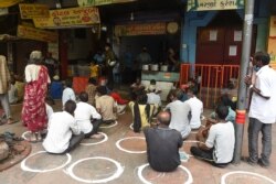 FILE - People in need sit while maintaining social distancing following COVID-19 Coronavirus guidelines, in front of a restaurant offering free meals in Ahmedabad, Sept. 19, 2020.