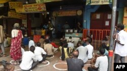 FILE - People in need sit while maintaining social distancing following COVID-19 Coronavirus guidelines, in front of a restaurant offering free meals in Ahmedabad, Sept. 19, 2020. 