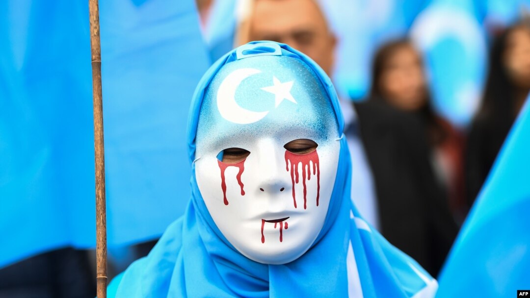 A person wearing a white mask with tears of blood takes part in a protest march of ethnic Uighurs during a demonstration around the EU institutions in Brussels.
