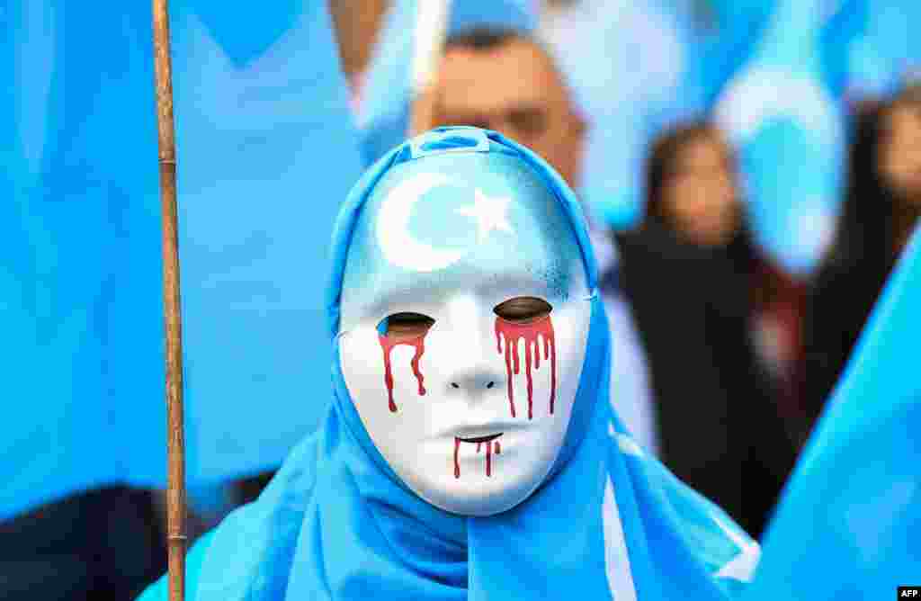 A person wearing a white mask with tears of blood takes part in a protest march of ethnic Uighurs during a demonstration around the EU institutions in Brussels.