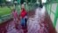 Beberapa warga berjalan melewati jalanan yang digenangi banjir berwarna merah karena bercampur dengan limbah sebuah pabrik batik di Pekalongan, Jawa Tengah, 6 Februari 2021. (Foto: Shaka/AFP)