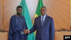 FILE— This picture taken and distributed by the Senegalese Presidency on March 28, 2024 shows outgoing Senegalese President Macky Sall (R) shaking hands with with Senegal's president-elect Bassirou Diomaye Faye (L) at the Presidential palace in Dakar.