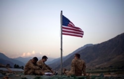 FILE - In this Sept. 11, 2011, photo, U.S. soldiers sit beneath an American flag raised to commemorate the tenth anniversary of the 9/11 attacks, at Forward Operating Base Bostick, in Kunar province, Afghanistan.