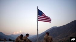 Tentara AS duduk di bawah bendera Amerika yang baru saja dikibarkan untuk memperingati sepuluh tahun serangan 9/11 di Pangkalan Operasi Maju Bostick di Provinsi Kunar, Afghanistan, 11 September 2011. (Foto: AP)