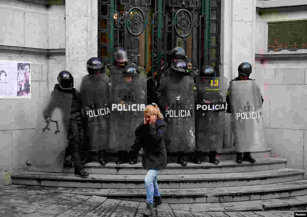 A pedestrian walks in front of riot policemen at the Bolivian Vice Presidency during a rally protest against Bolivia&#39;s government new health care policies in La Paz, Jan. 8, 2018.