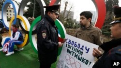 Activist David Khakim (C) is approached by two police officers after pulling out a banner protesting a recent prison sentence for a local environmentalist in front of the Olympic rings, Feb. 17, 2014, in central Sochi, Russia.