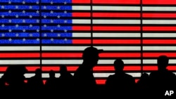 ARCHIVO - Varias personas se congregan frente a unas pantallas que muestran la bandera estadounidense en Times Square, Nueva York, el 9 de agosto de 2024.