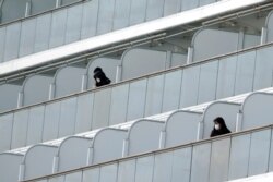 Masked passengers stand outside on the balcony of the cruise ship Diamond Princess anchored at Yokohama Port in Yokohama, near Tokyo, Feb. 7, 2020.