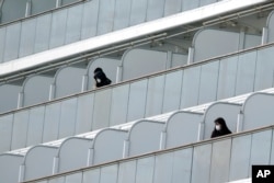 Masked passengers stand outside on the balcony of the cruise ship Diamond Princess anchored at Yokohama Port in Yokohama, near Tokyo, Feb. 7, 2020.