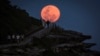 A super moon rises behind people standing on a headland near Sydney&#39;s Bondi Beach, Australia.