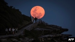 A super moon rises behind people standing on a headland near Sydney&#39;s Bondi Beach, Australia.