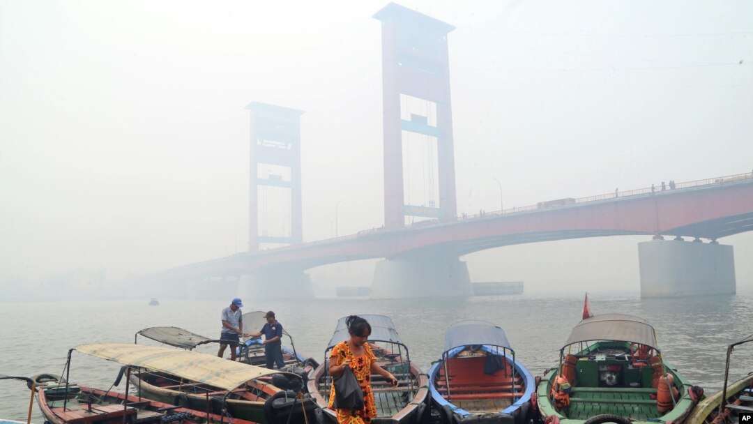 Seorang perempuan di atas kapal dekat Jembatan Ampera di Palembang yang diselimuti kabut asap kebakaran hutan, Palembang, Sumatra Selatan, 29 September 2015. (Foto: AP)