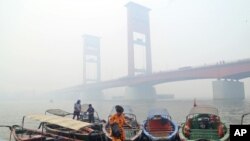 Seorang perempuan di atas kapal dekat Jembatan Ampera di Palembang yang diselimuti kabut asap kebakaran hutan, Palembang, Sumatra Selatan, 29 September 2015. (Foto: AP)