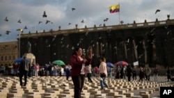 Una mujer de pie entre cajas que representan féretros, mientras rinde tributo a antiguos guerrilleros y líderes sociales asesinados, desde que se firmó un acuerdo de paz en 2016 entre rebeldes de las FARC y el gobierno colombiano, el martes 20 de febrero de 2024, en Bogotá. 