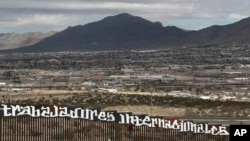 Sunland Park, New Mexico, is seen over the U.S. border fence as a protester finishes painting the Spanish slogan "Neither delinquents nor illegals, we are international workers" on the Anapra, Mexico, side of the fence, Feb. 26, 2017. 