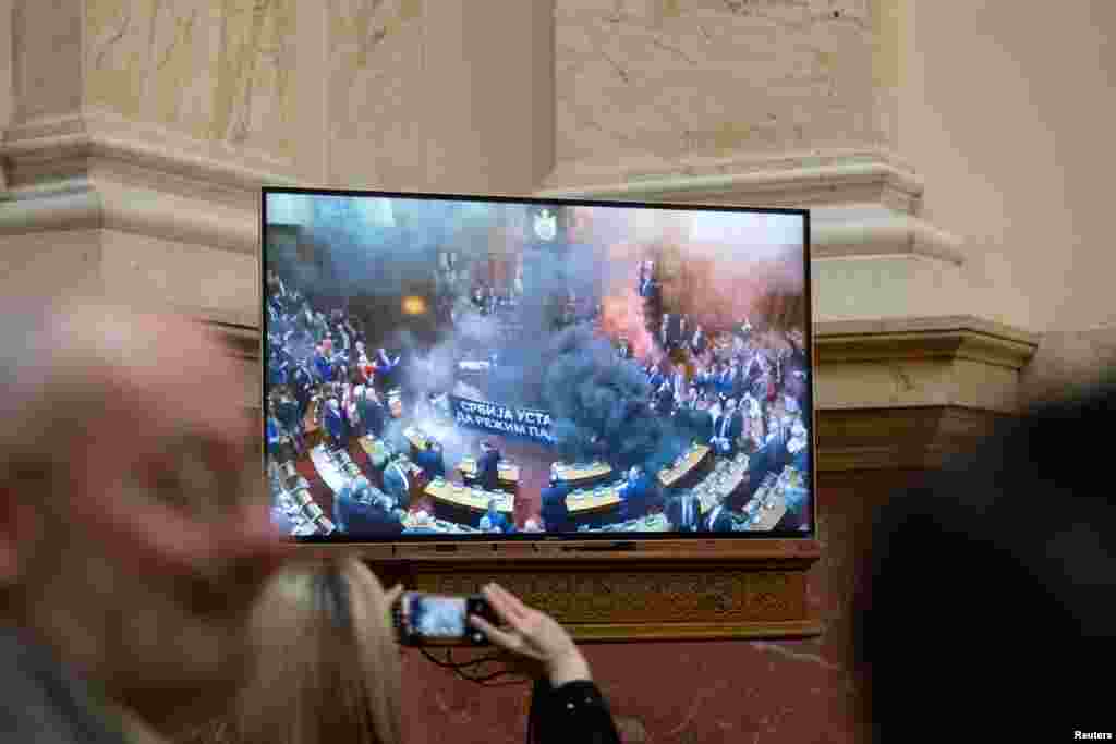 Journalists watch live broadcast while opposition members of parliament let off smoke grenade inside Serbian parliament, in Belgrade.