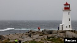 Two Royal Canadian Mounted Police officers walk toward the Peggy's Cove Lighthouse to warn individuals of the dangers during the arrival of Hurricane Dorian in Peggy's Cove, Nova Scotia, Sept. 7, 2019.