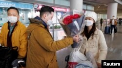 Seorang pria memberikan bunga kepada seorang perempuan usai melewati gerbang kedatangan internasional di Bandara Internasional Beijing setelah China melonggarkan aturan COVID-19 bagi pelancong internasional, Minggu 8 Januari 2023. 