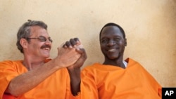 FILE - James Gatdet Dak, right, clasps hands with William Endley, left, a South African former defense colonel who also worked with the opposition, as they prepare to be released from prison after their death sentence was pardoned, in Juba, South Sudan, Friday, Nov. 2, 2018. 