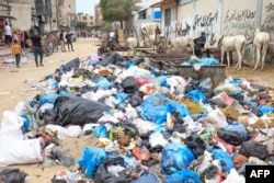 FILE - Palestinians walk amid piles of rubbish littering a street in Khan Yunis in the southern of Gaza Strip, on October 16, 2023.