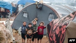 FILE - Children look on as they stand next to a tent at a flooded camp for Syrians displaced by conflict near the village of Kafr Uruq, in Syria's northern rebel-held Idlib province, Jan. 17, 2021. 