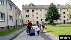 Four-year-old refugee Lilas from Syria and her parents walk to their refugee home in Muelheim an der Ruhr, Germany, after receiving articles for daily use prepared by donors at a distribution center, Aug, 20, 2015. 