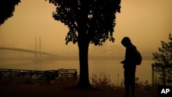 A person rides a skateboard along the Willamette River as smoke from wildfires partially obscures the Tilikum Crossing Bridge, Sept. 12, 2020, in Portland, Ore. 