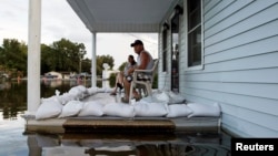 Megan Schexnayder dan David McNeely duduk di teras rumah mereka di Sorrento, Lousiana yang dikepung banjir (17/8). (Reuters/Edmund D. Fountain)