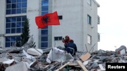 Seorang anggota SAR memasang bendera Albania selama pencarian korban di sebuah gedung yang runtuh di Durres, setelah gempa bumi mengguncang Albania, 28 November 2019. (Foto: Reuters/Florion Goga)