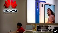 A sales clerk looks at his smartphone in a Huawei store at a shopping mall in Beijing Wednesday, July 4, 2018. 