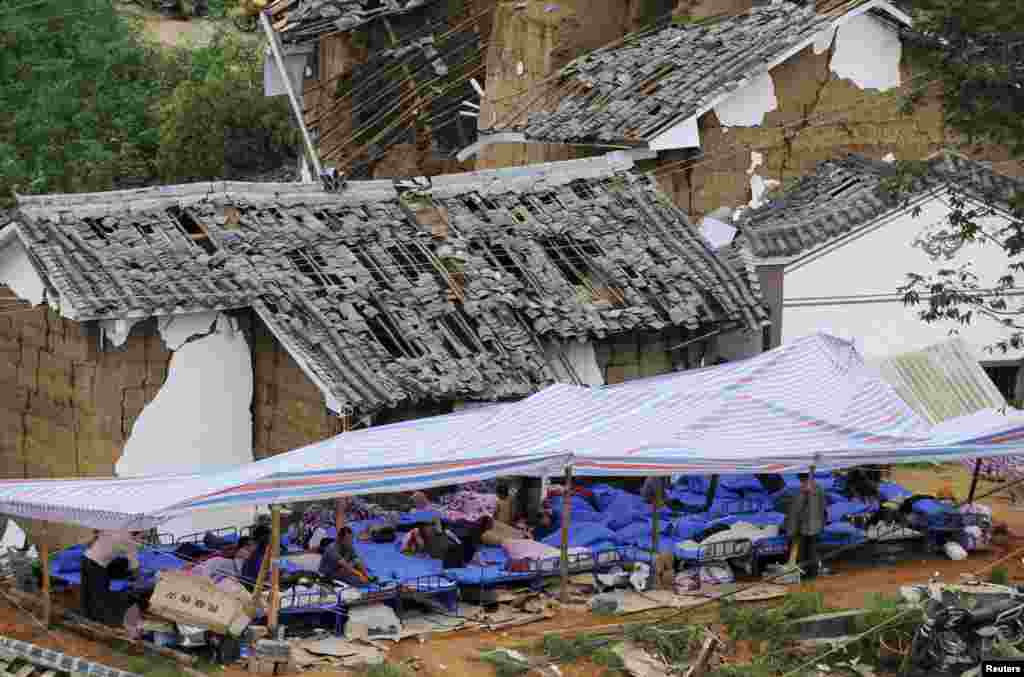 Villagers rest under a makeshift tent next to damaged houses in Ludian county, Zhaotong, Yunnan province, Aug. 4, 2014.