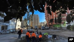People watch as rescuers search in a destroyed building in Adana, southeastern Turkey, Thursday, Feb. 9, 2023. 