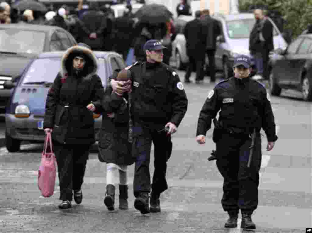 A student, second from left, is flanked by an unidentified woman and police officers as they leave a Jewish school after a gunman opened fire in Toulouse, southwestern France, Monday, March 19, 2012. A father and his two sons were among four people who di