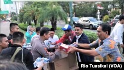 Ketua Relawan Golkar Jokowi (gojo) Rizal Mallarangeng (kanan) memimpin timnnya membagikan makanan cepat saji kepada petugas yang berjaga di sekitar Gedung KPU, Kamis sore, 23 Mei 2019. (Foto: Rio Tuasikal/VOA)