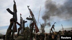 FILE - Rebel fighters hold up their rifles as they walk in front of a bushfire in a rebel-controlled territory in Upper Nile State, South Sudan February 13, 2014.