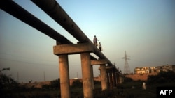 FILE - Men carry jerry cans as they walk along a pipeline in Karachi, Pakistan, on May 2014.