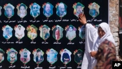 An Afghan woman cries as she touches a banner displaying photographs of victims of the recent wedding hall bombing during a memorial service in Kabul, Afghanistan, Aug. 20, 2019.